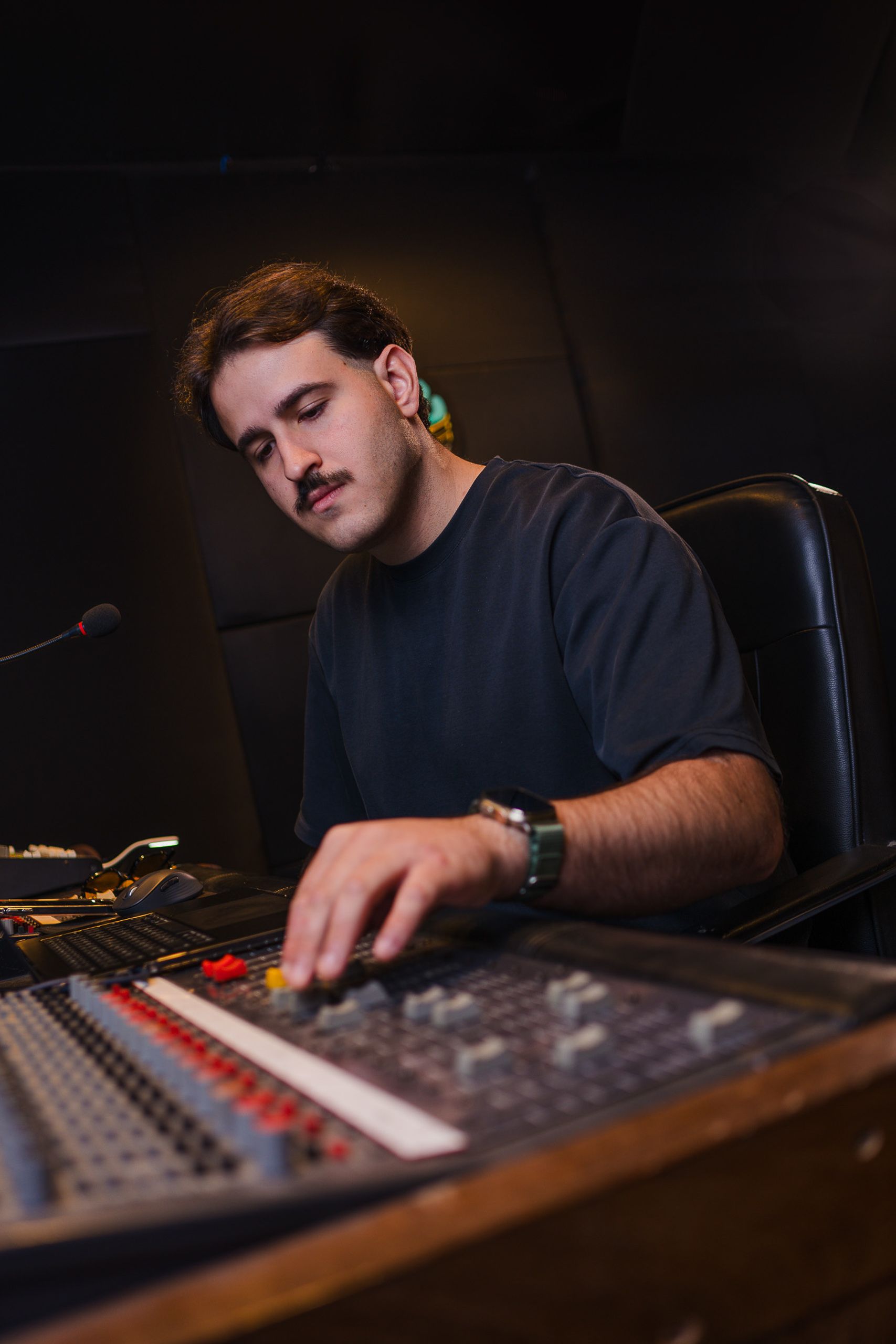 Produtor musical ajustando os controles da mesa de som, em estúdio de luz baixa.