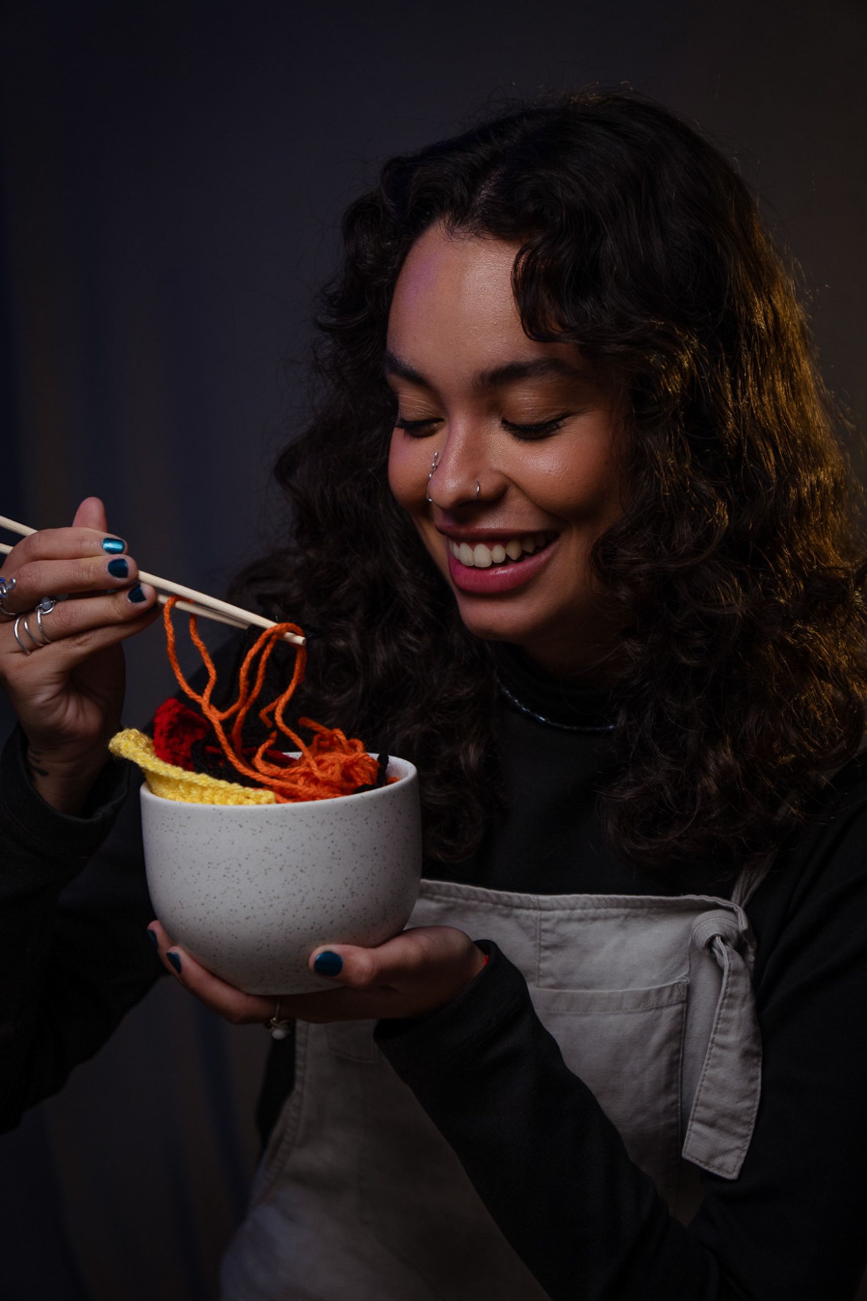 Fotografia profissional de professora de crochê segurando tigela com macarrão de crochê e hashis.