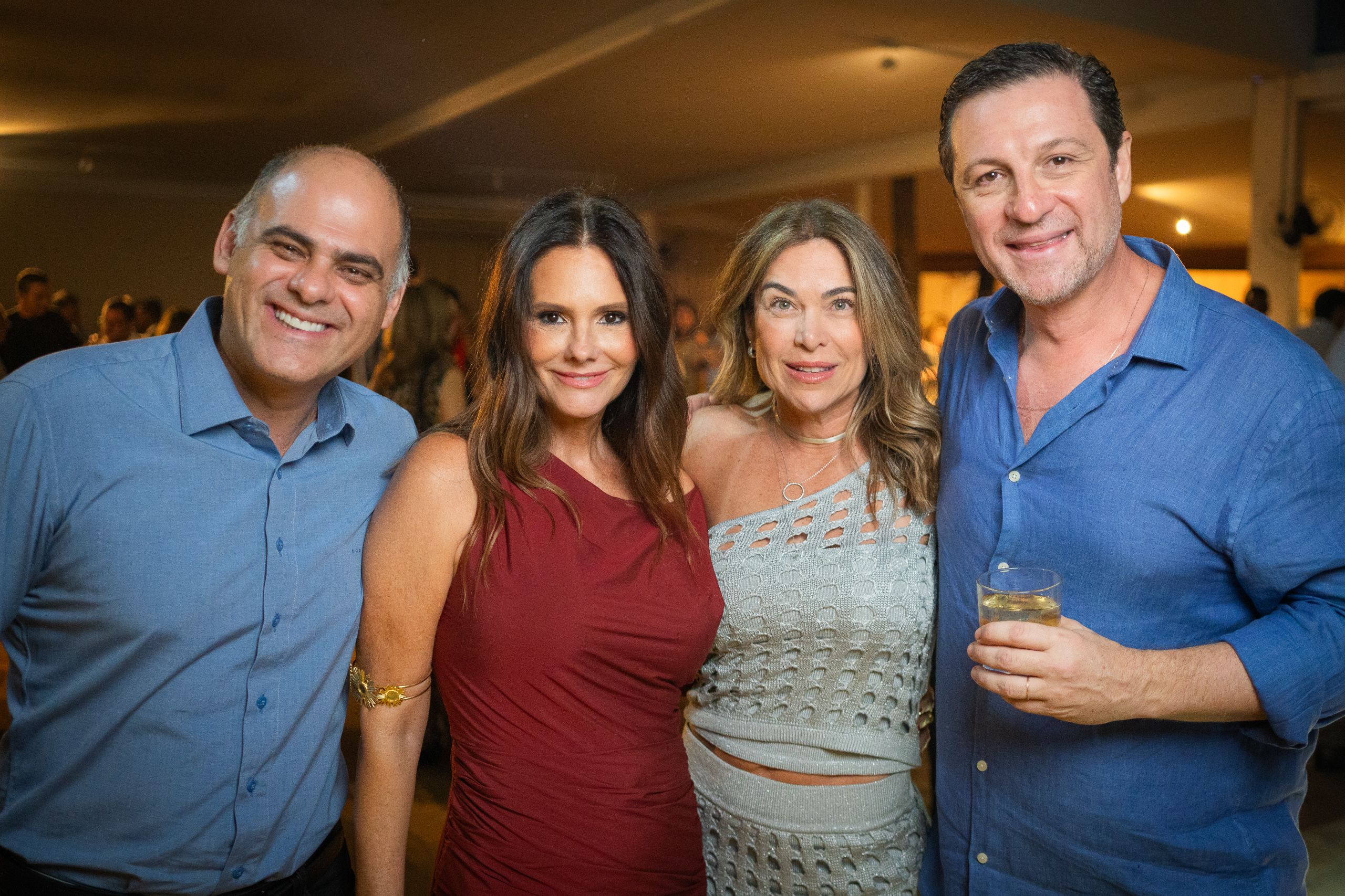 Quatro convidados posando juntos em uma festa, um deles segurando um copo.