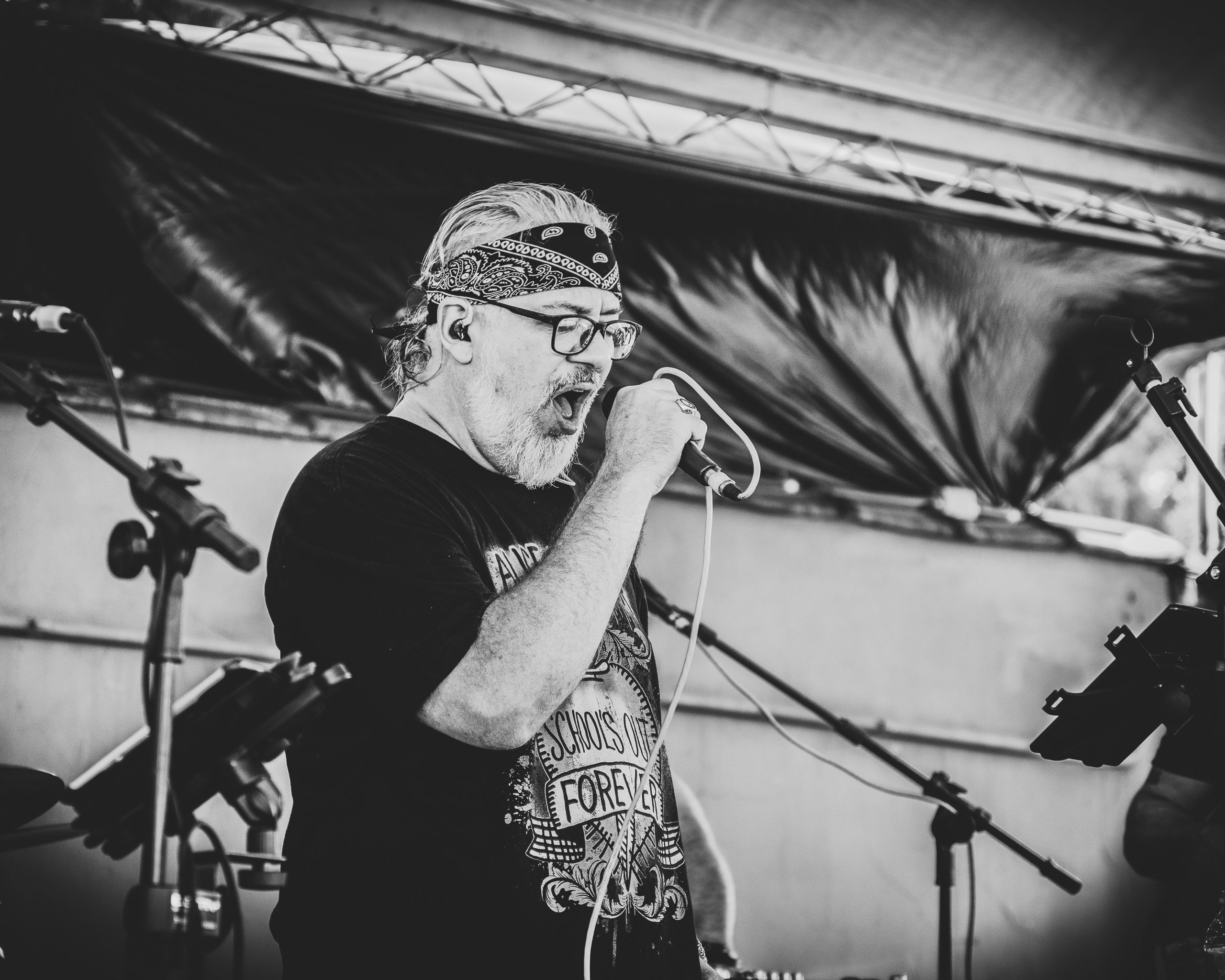 Homem de bandana cantando ao microfone em palco, registrado em preto e branco.